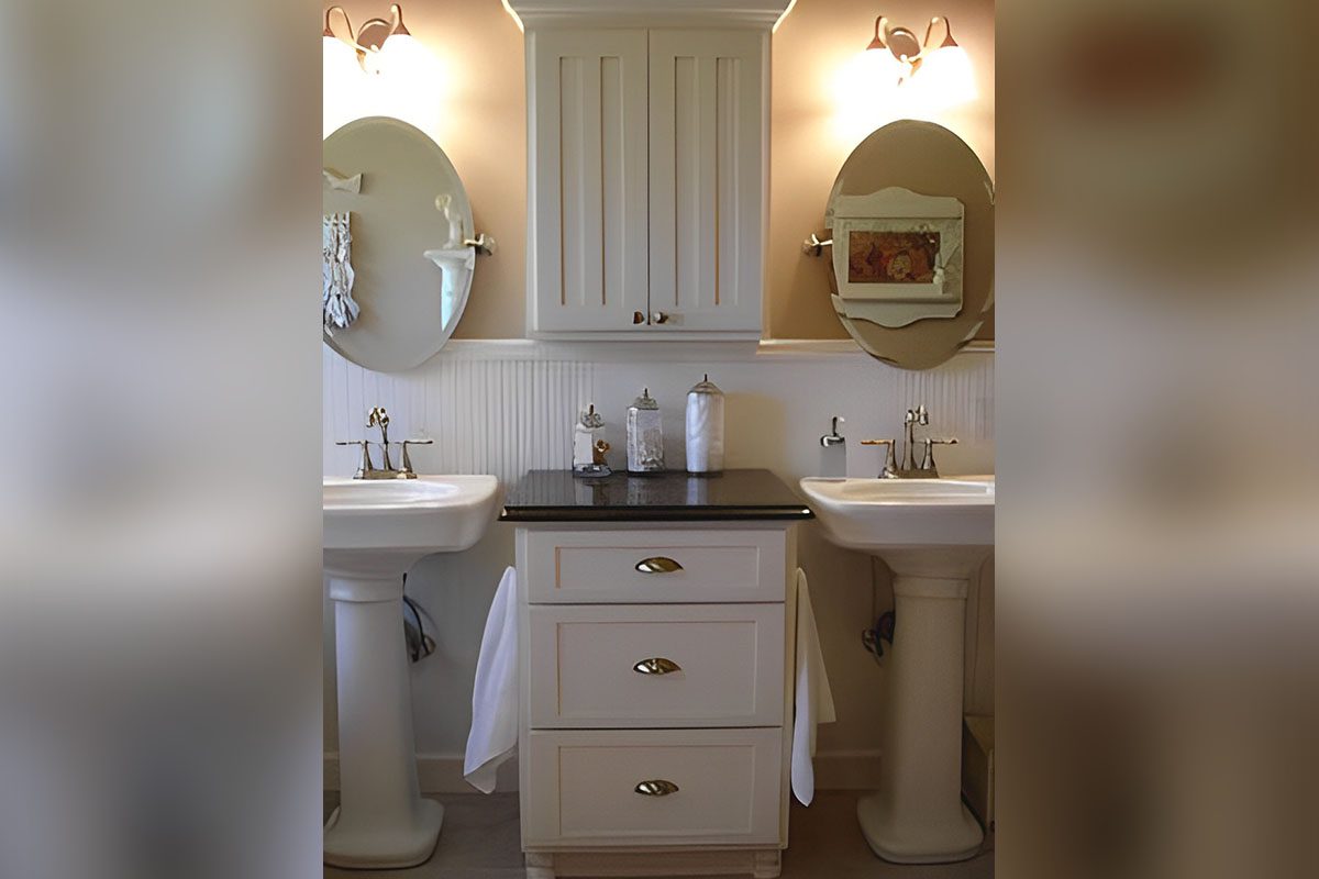 A bathroom features two pedestal sinks with oval mirrors above, a central cabinet with drawers, and wall-mounted lights.