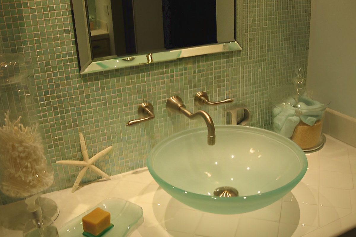 A bathroom featuring a glass vessel sink, metallic faucet, mosaic tile backsplash, starfish decoration, and soap dish. A candle and folded towels are visible on the counter.
