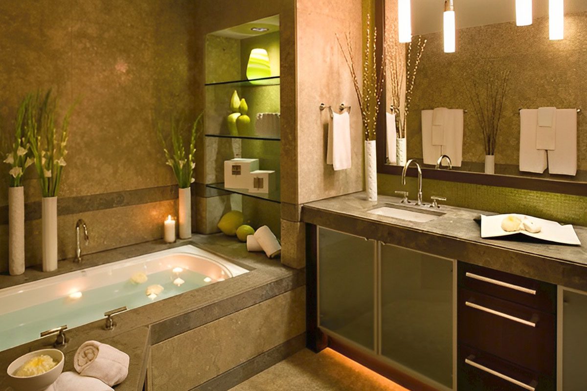 A modern bathroom with a lit bathtub, dual sinks, and a large mirror. Towels are neatly arranged, and the decor includes plants, candles, and recessed lighting.
