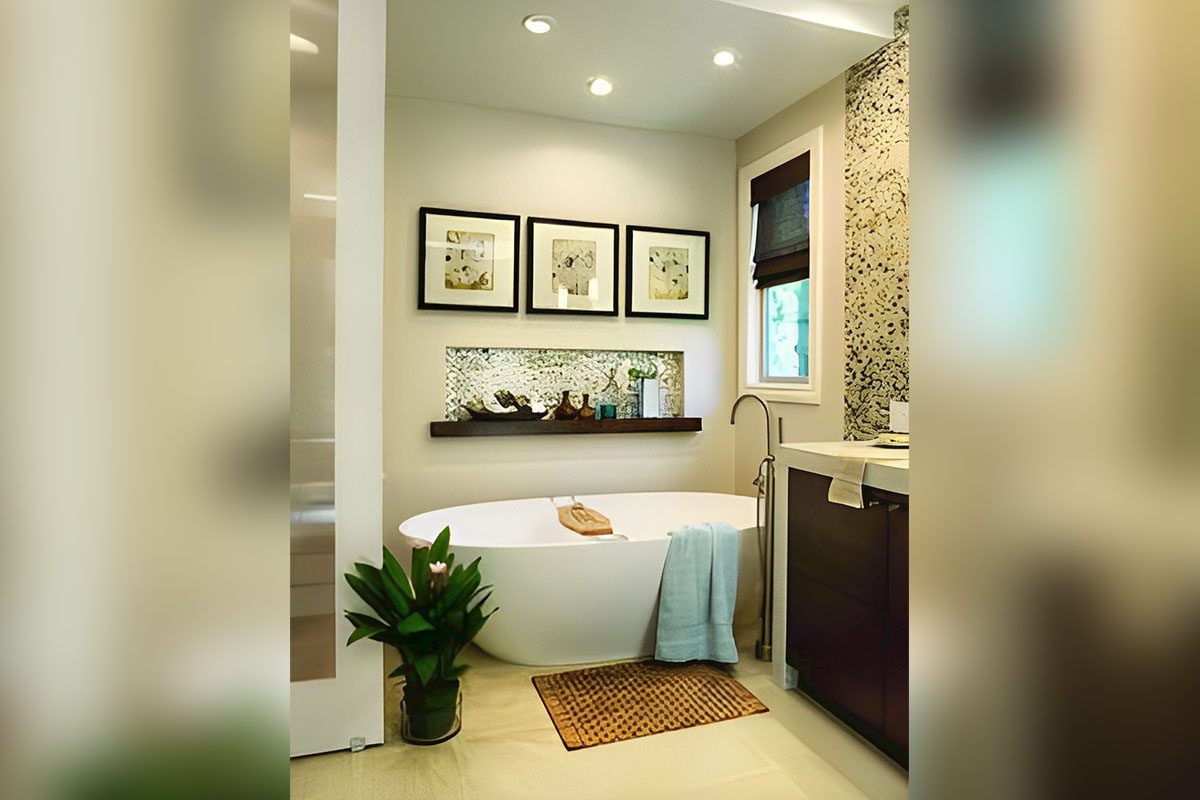Modern bathroom with a white oval bathtub, three framed pictures above, a shelf with decor, a potted plant, and a patterned rug. Natural light comes through a small window with a blind.