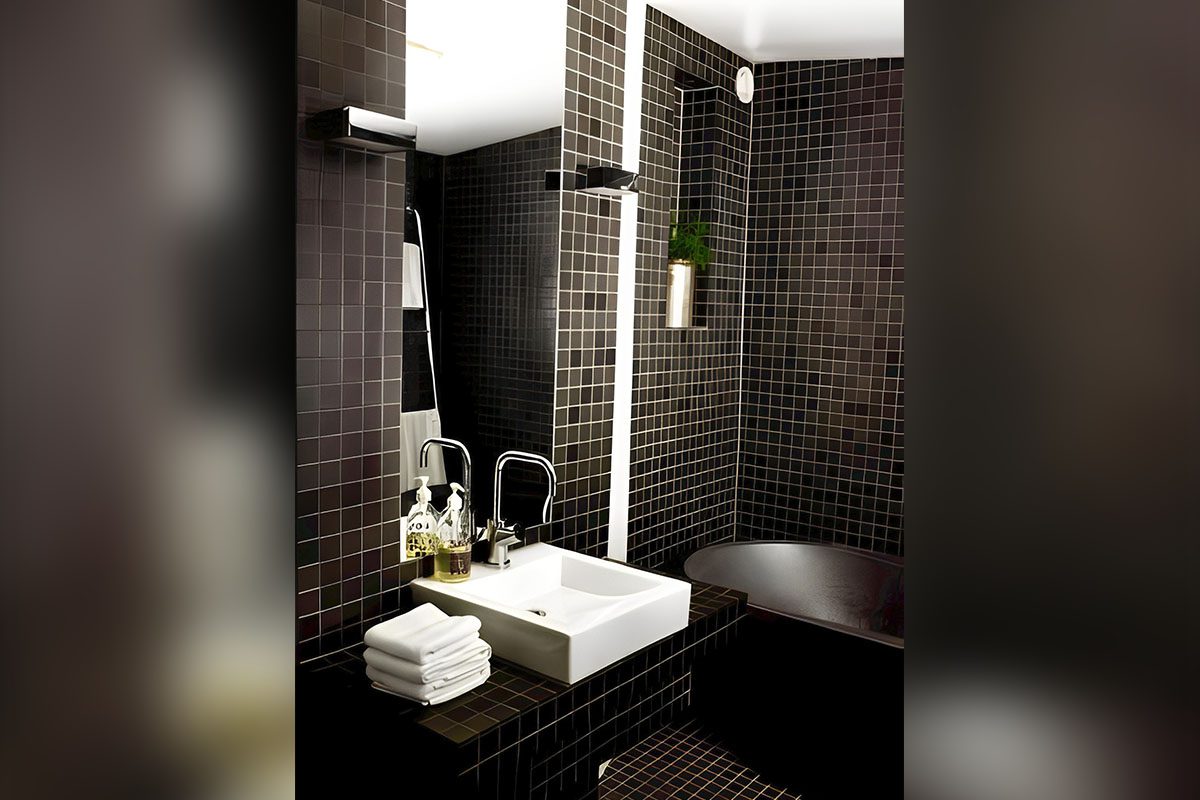 Modern bathroom with black tiled walls, a white square sink with soap dispensers and folded towels, a mirror above, a bathtub, and a small potted plant on the wall.
