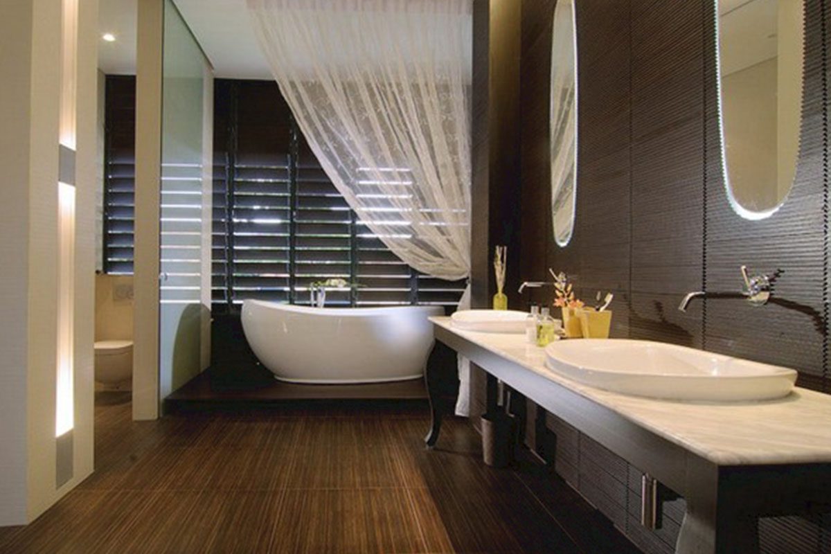 Modern bathroom with dark wood paneling, featuring a freestanding bathtub by a window with vertical blinds, dual sinks on a marble countertop, and a large mirror.
