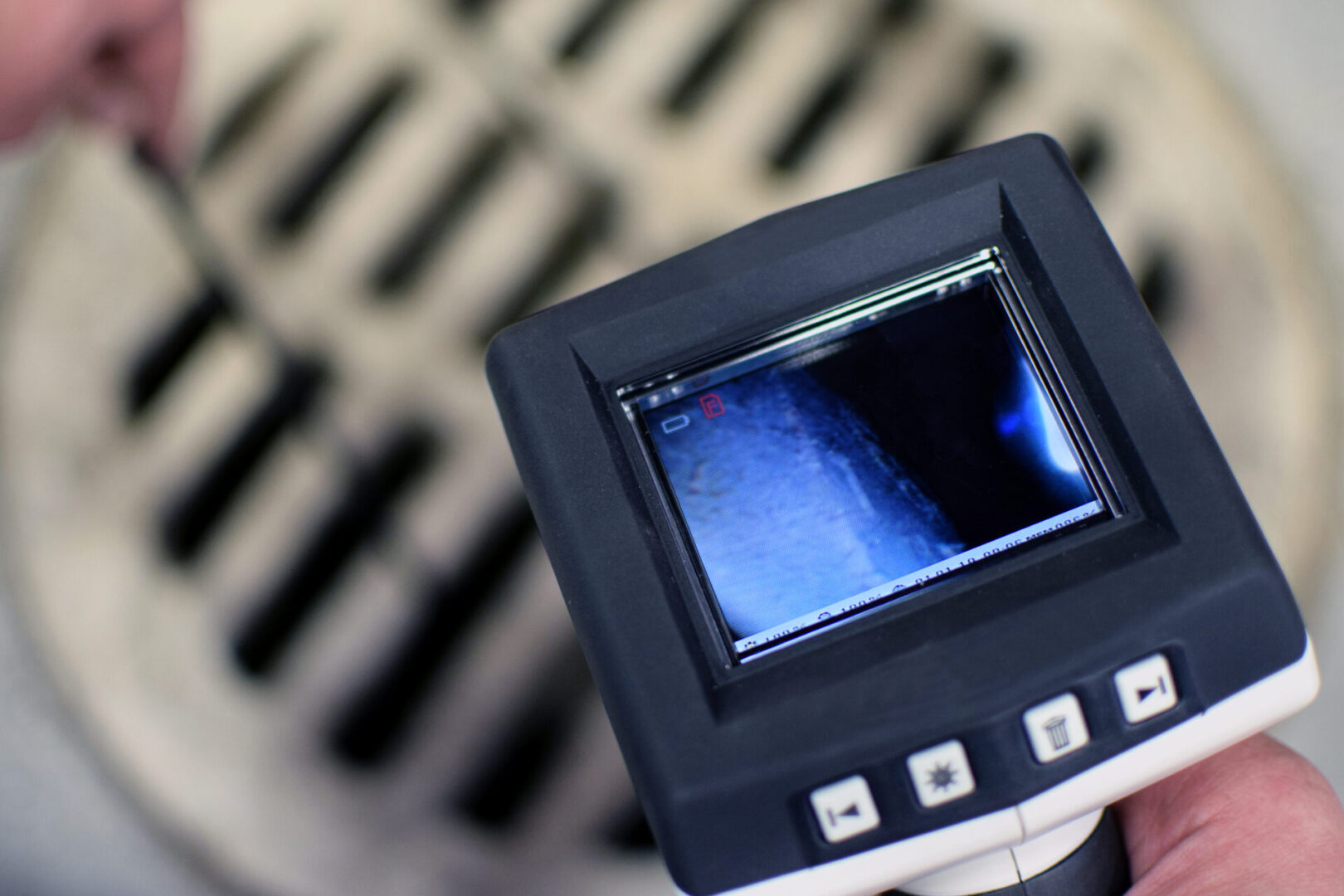 Person using a camera with a display screen to inspect inside a round vent or drain cover.